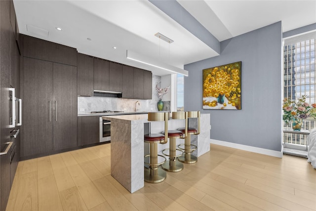 kitchen featuring a kitchen breakfast bar, light wood-type flooring, tasteful backsplash, stainless steel appliances, and sink