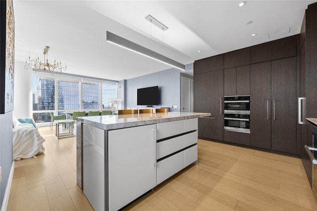 kitchen with an inviting chandelier, hanging light fixtures, light hardwood / wood-style flooring, a kitchen island, and stainless steel double oven