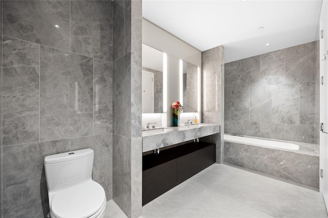 bathroom with a washtub, vanity, tile walls, and toilet