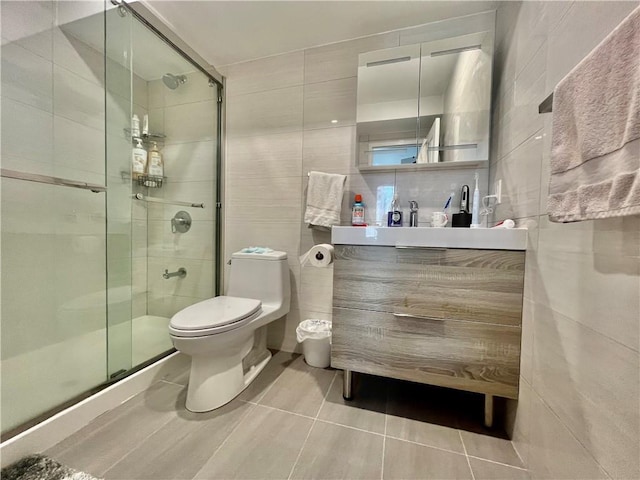 bathroom featuring tile patterned flooring, toilet, a shower with door, vanity, and tile walls