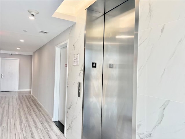 corridor with elevator and light hardwood / wood-style flooring