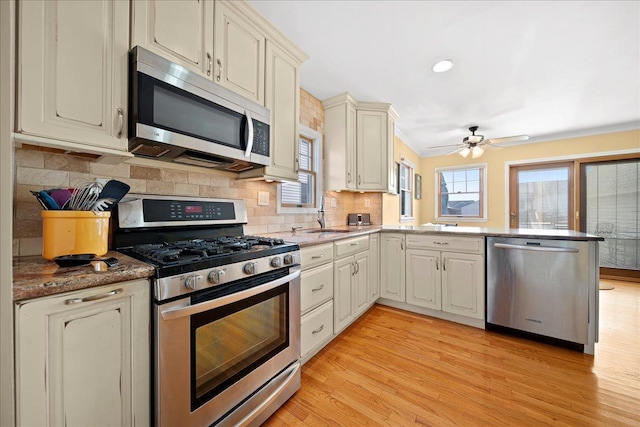 kitchen with sink, stainless steel appliances, kitchen peninsula, light wood-type flooring, and ornamental molding