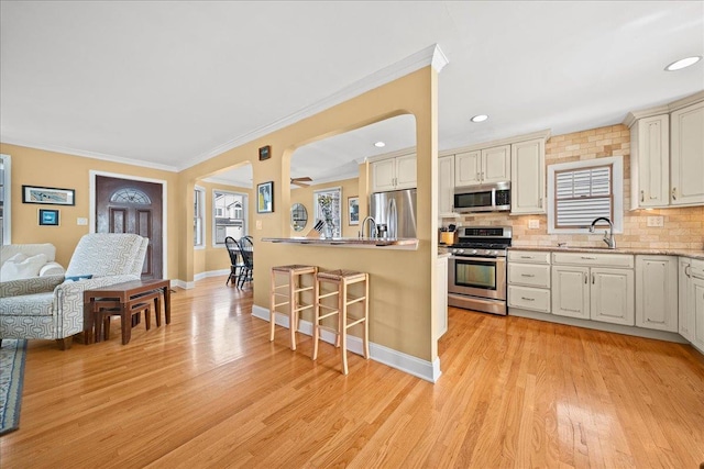 kitchen featuring sink, stainless steel appliances, crown molding, decorative backsplash, and light wood-type flooring