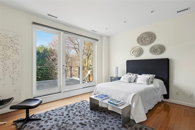 bedroom featuring access to outside, multiple windows, wood-type flooring, and baseboard heating