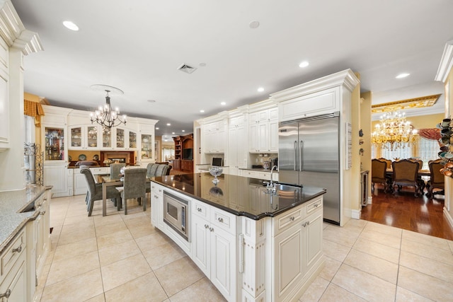 kitchen featuring an inviting chandelier, white cabinets, light hardwood / wood-style flooring, built in appliances, and an island with sink