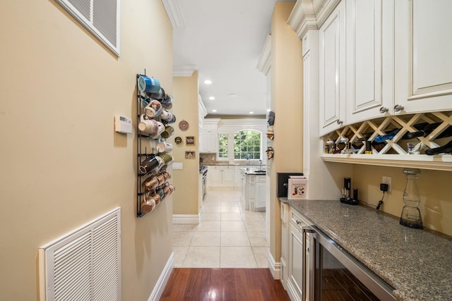 bar with dark stone counters, white cabinets, wine cooler, light tile patterned floors, and ornamental molding