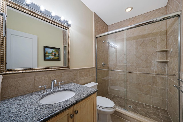 bathroom with vanity, toilet, tile walls, and a shower with shower door