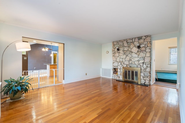 unfurnished living room featuring hardwood / wood-style flooring, a stone fireplace, crown molding, and a baseboard radiator