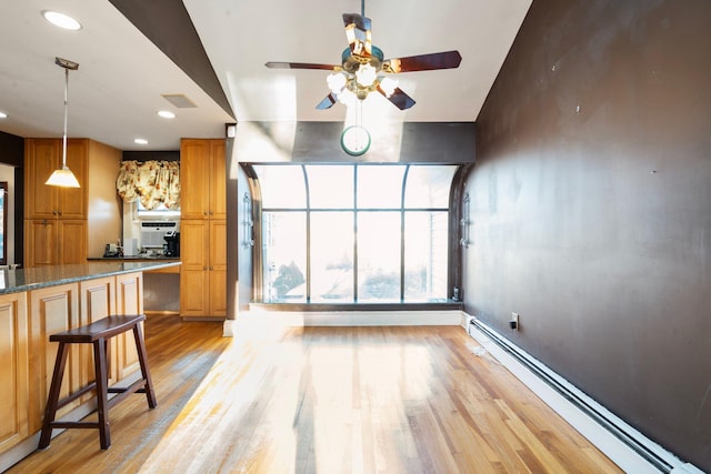 interior space featuring light stone countertops, light wood-type flooring, a breakfast bar, ceiling fan, and a baseboard heating unit