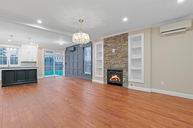 unfurnished living room featuring built in shelves, light hardwood / wood-style flooring, a wealth of natural light, and an AC wall unit