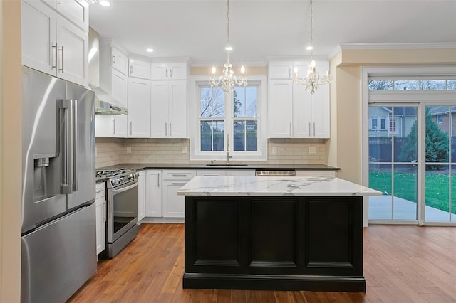 kitchen with stainless steel appliances, wall chimney range hood, sink, an inviting chandelier, and white cabinets