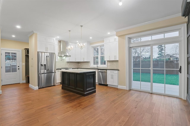 kitchen featuring wall chimney range hood, hanging light fixtures, light wood-type flooring, a kitchen island, and stainless steel appliances