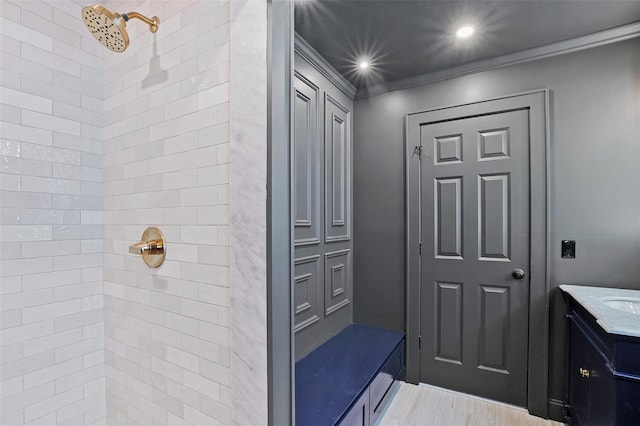 bathroom with wood-type flooring, vanity, a tile shower, and ornamental molding