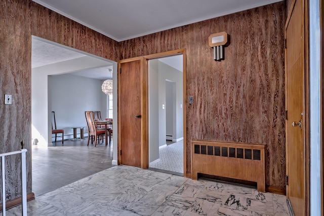 corridor featuring a baseboard heating unit, radiator, wood walls, and an inviting chandelier