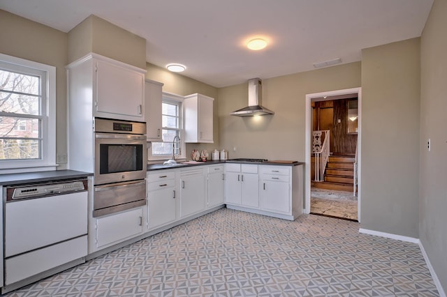 kitchen with stainless steel appliances, sink, white cabinets, and wall chimney range hood