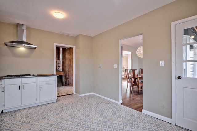 kitchen with stainless steel gas cooktop, light hardwood / wood-style floors, white cabinets, and wall chimney range hood