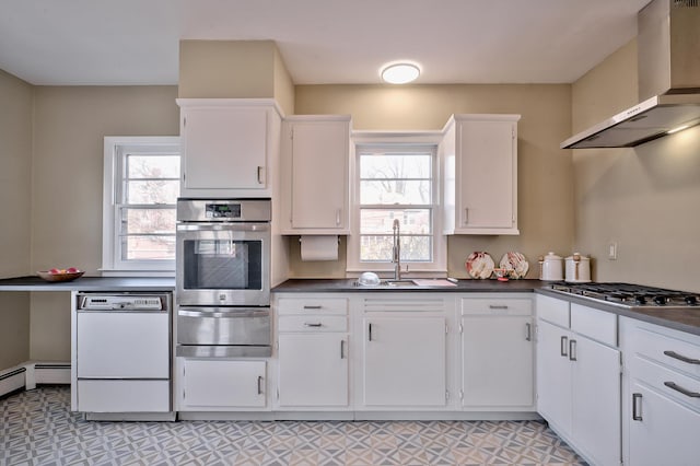 kitchen with a healthy amount of sunlight, appliances with stainless steel finishes, wall chimney exhaust hood, and white cabinets