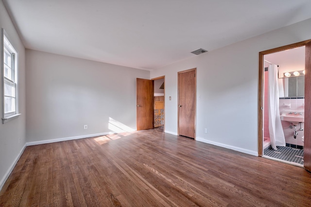 unfurnished bedroom with sink, connected bathroom, dark hardwood / wood-style floors, and multiple windows