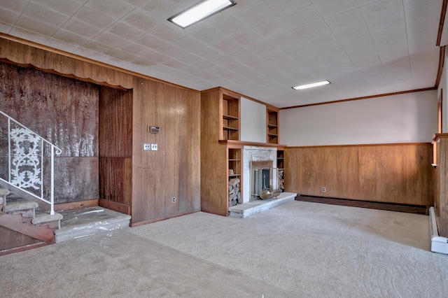 unfurnished living room with light colored carpet, ornamental molding, a stone fireplace, and wooden walls