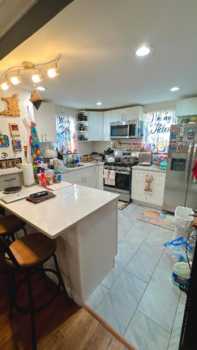 kitchen featuring a kitchen bar, kitchen peninsula, white cabinetry, and appliances with stainless steel finishes