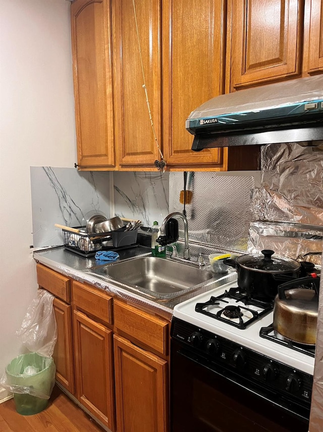 kitchen featuring wood-type flooring, backsplash, white range with gas cooktop, and sink