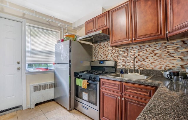 kitchen featuring radiator, sink, stainless steel gas range oven, backsplash, and dark stone counters