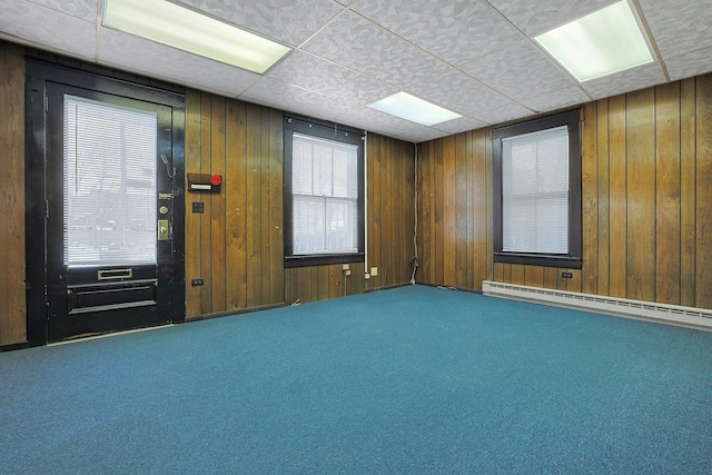 unfurnished room featuring carpet flooring, a paneled ceiling, wood walls, and a baseboard radiator