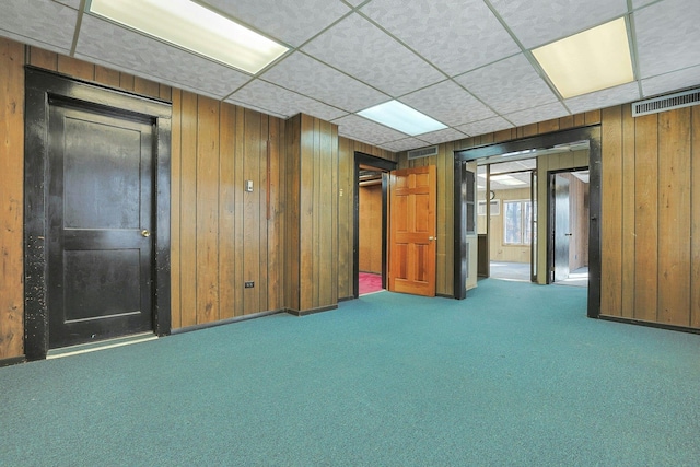 basement with carpet, a paneled ceiling, and wood walls