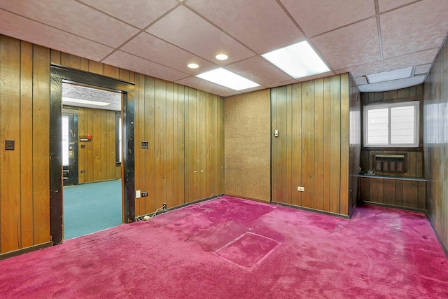 carpeted spare room featuring a paneled ceiling and wooden walls