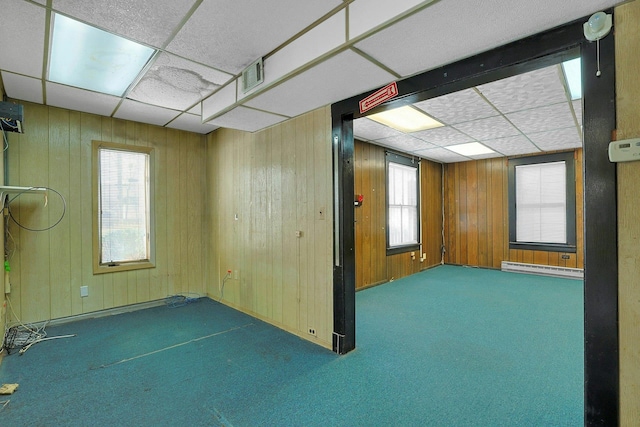 empty room with a wealth of natural light, carpet floors, a baseboard radiator, and wood walls