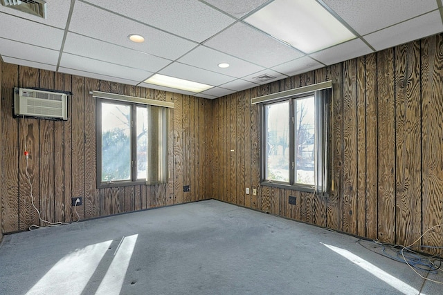 carpeted empty room featuring a wall mounted air conditioner, a drop ceiling, and a healthy amount of sunlight