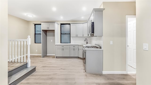 kitchen with white range oven, gray cabinetry, sink, and light hardwood / wood-style floors