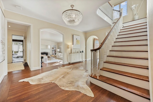 entryway featuring dark wood-type flooring, crown molding, and a notable chandelier