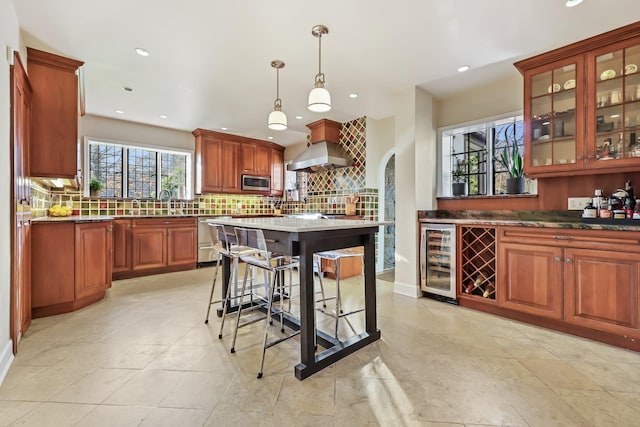 kitchen featuring wine cooler, island range hood, hanging light fixtures, stainless steel appliances, and decorative backsplash