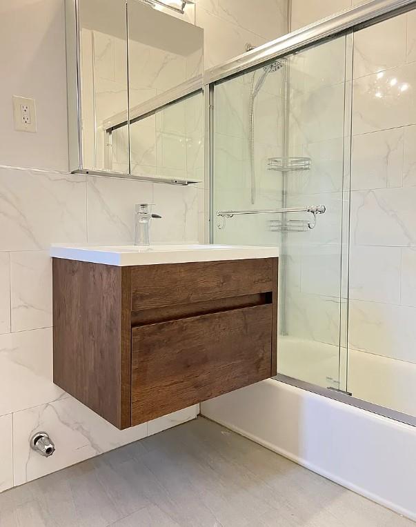 bathroom featuring combined bath / shower with glass door, vanity, and tile walls