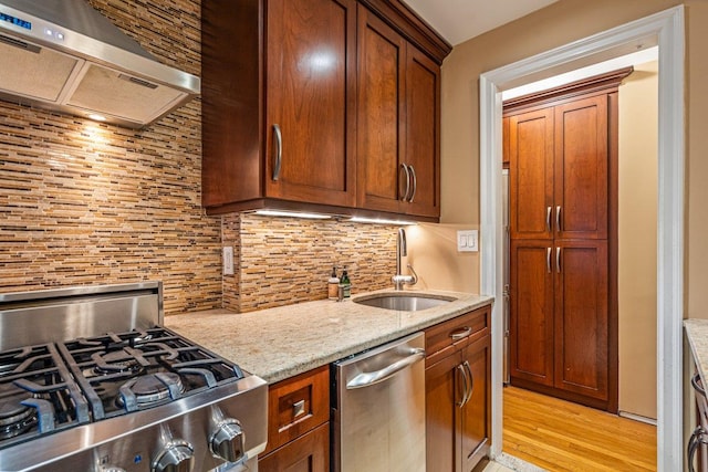 kitchen featuring backsplash, exhaust hood, sink, light stone countertops, and appliances with stainless steel finishes