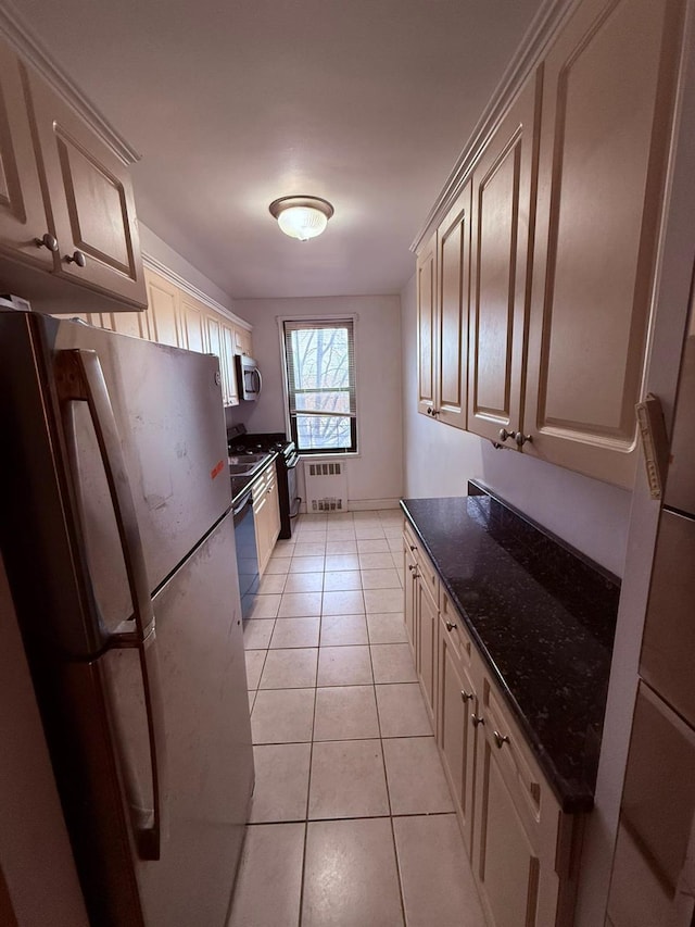 kitchen with dishwasher, dark stone countertops, light tile patterned floors, fridge, and radiator heating unit