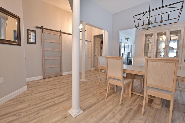 dining area featuring light wood-type flooring, a barn door, a chandelier, and decorative columns