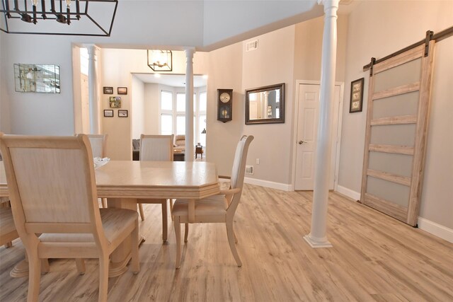 dining area with a high ceiling, a barn door, light hardwood / wood-style floors, and an inviting chandelier