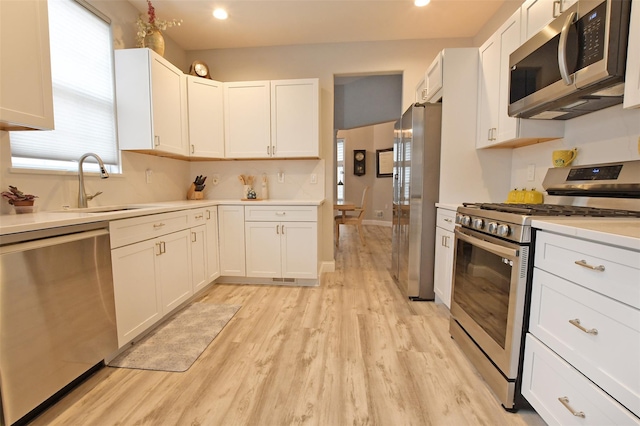 kitchen with light wood-type flooring, stainless steel appliances, white cabinetry, and sink