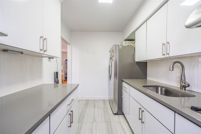 kitchen featuring stainless steel refrigerator, white cabinetry, sink, backsplash, and light tile patterned floors