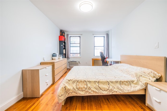 bedroom featuring a wall unit AC, radiator heating unit, and wood-type flooring