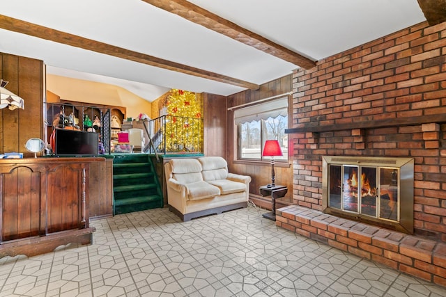 living room featuring beam ceiling, a brick fireplace, and wood walls