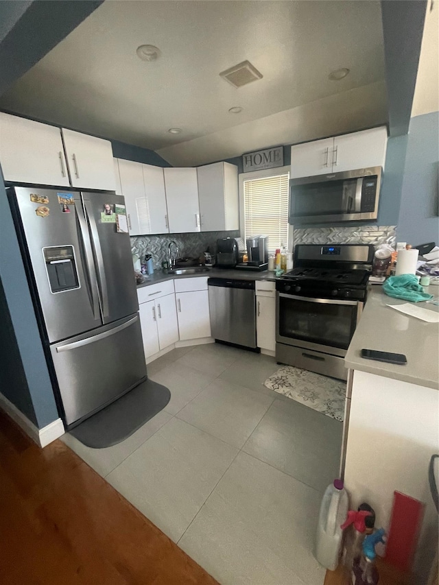 kitchen featuring tasteful backsplash, sink, white cabinetry, stainless steel appliances, and light tile patterned floors