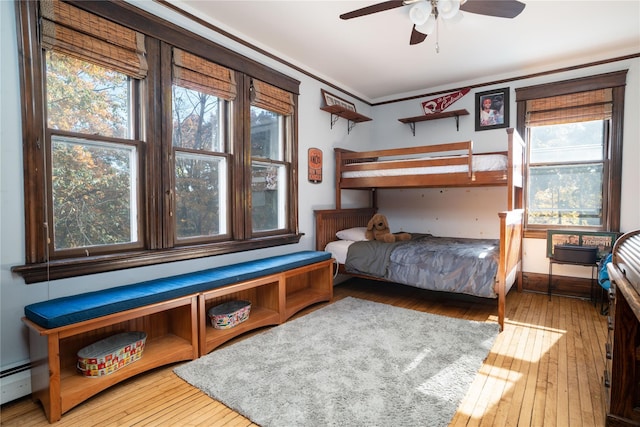 bedroom with ceiling fan, wood-type flooring, baseboard heating, and multiple windows