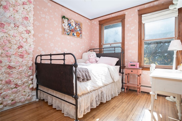 bedroom with hardwood / wood-style floors, a baseboard radiator, and ornamental molding