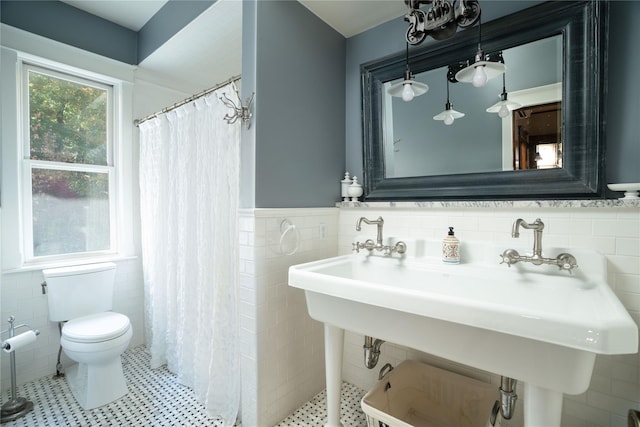 bathroom featuring a sink, a tile shower, tile walls, wainscoting, and toilet