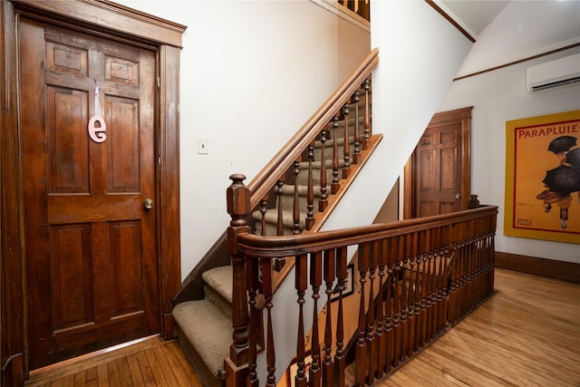 stairway featuring hardwood / wood-style flooring, baseboards, lofted ceiling, and a wall unit AC