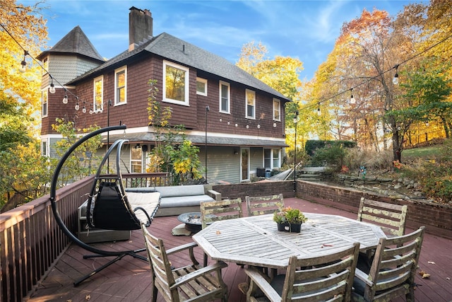 rear view of house featuring outdoor dining space, roof with shingles, a chimney, and a deck