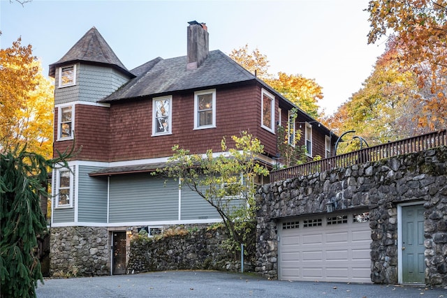 rear view of house featuring stone siding, an attached garage, a chimney, and aphalt driveway